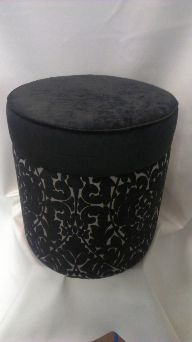 A round ottoman upholstered in black damask flock and velvet