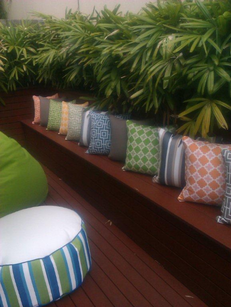 A row of patterned scatter cushions along a timber deck bench