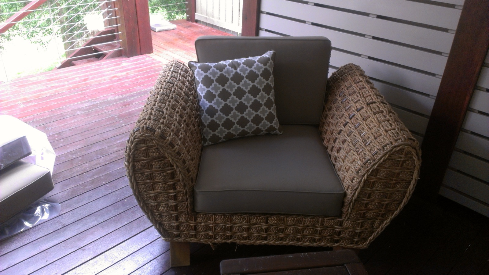 An outdoor wicker armchair with a new taupe cushion